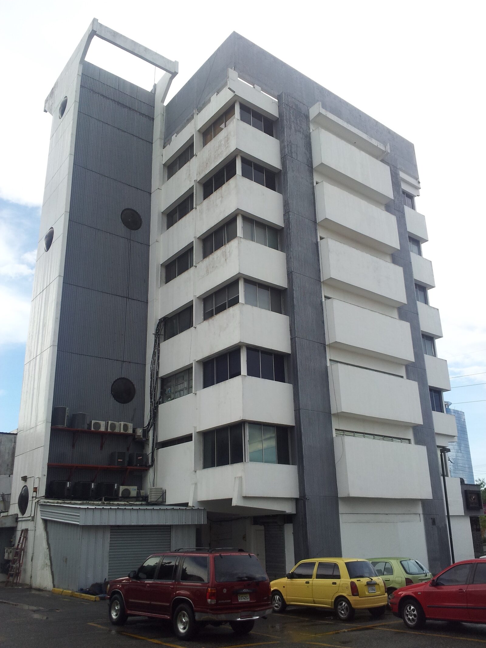 Núcleo de circulación original del edificio W69 antes de la renovación, con fachada de concreto y área de estacionamiento al frente.