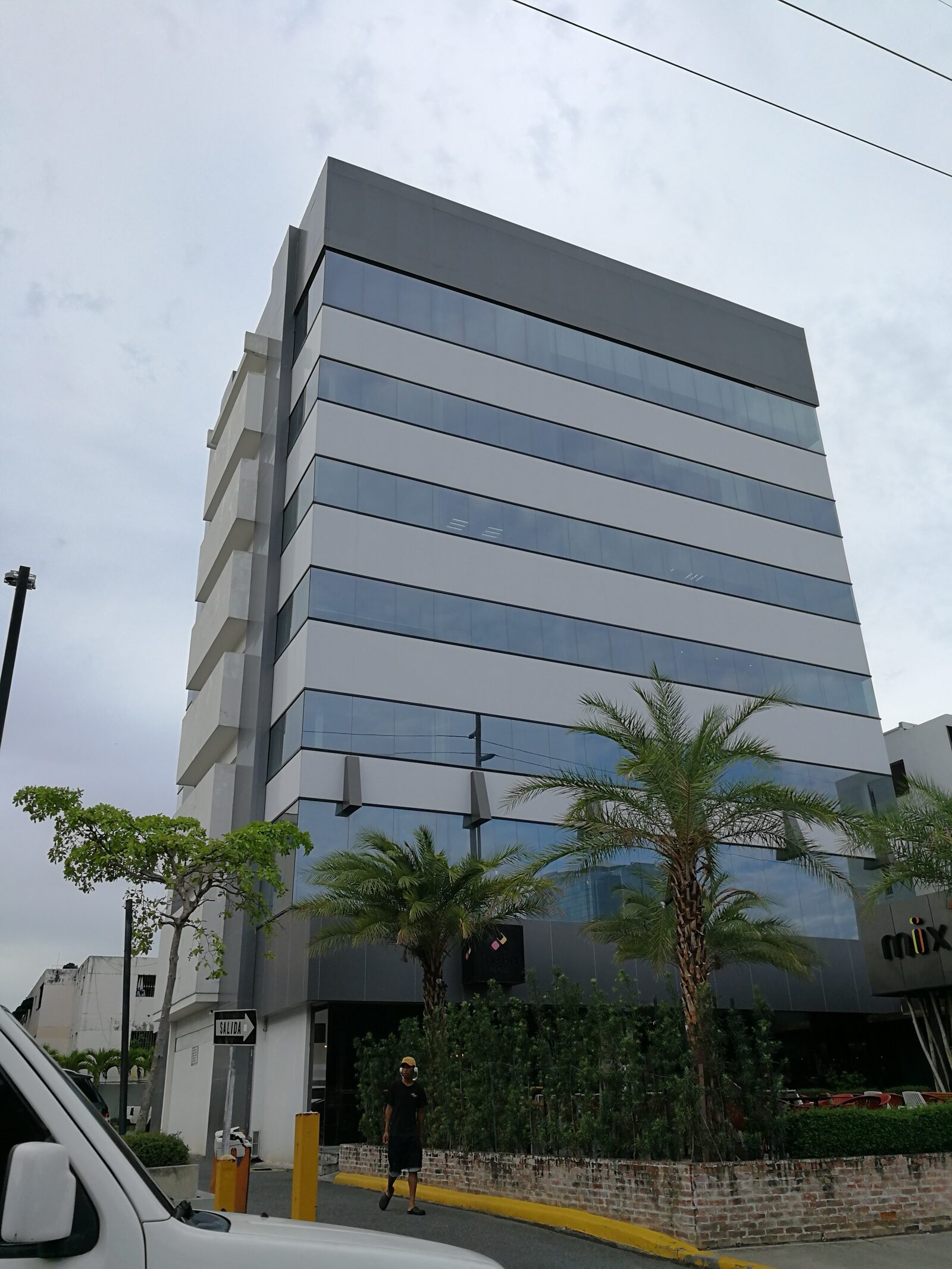 Fotografía del edificio W69 terminado, vista de esquina con la nueva fachada de paneles metálicos, vidrio y palmeras en la acera.